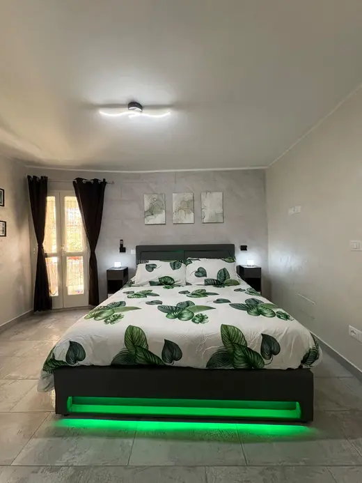 Camera matrimoniale con lenzuola a foglie verdi e luci LED sotto il letto