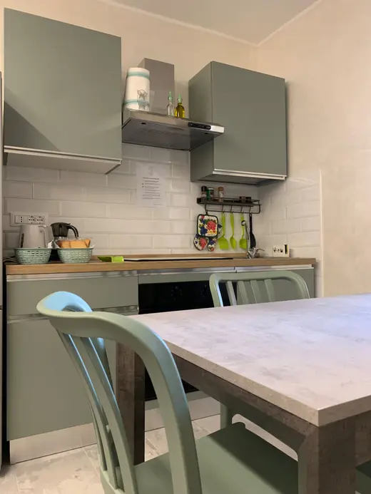 Cucina con pensili verde salvia, piano in legno e tavolo da pranzo